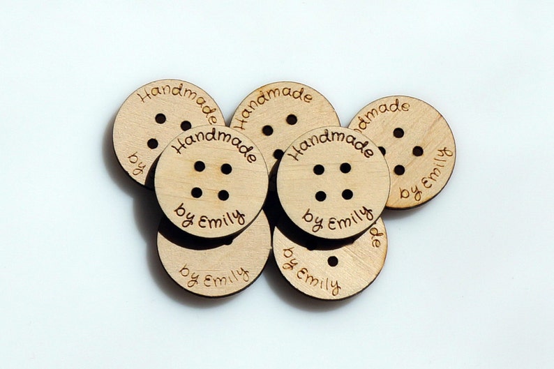 May include: A close-up of six round wooden buttons with the text "Handmade by Emily" engraved on each button.