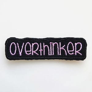 May include: Black felt patch with pink embroidered text that reads "overthinker".