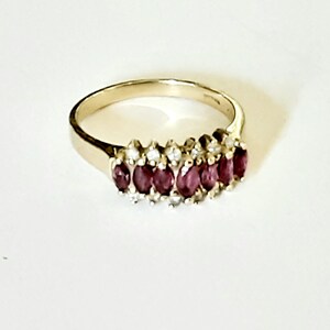 May include: A gold band ring with a row of oval-shaped ruby stones set in a pave setting with smaller diamonds.