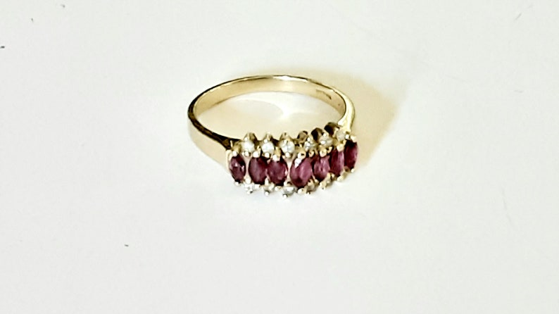 May include: A gold band ring with a row of oval-shaped ruby stones set in a pave setting with smaller diamonds.