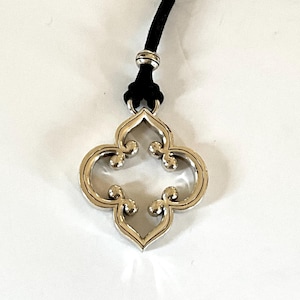 May include: A silver-toned pendant necklace with a four-leaf clover design. The pendant is suspended from a black cord. The necklace is displayed against a white background.
