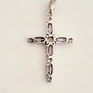 Pu&ograve; includere: Un ciondolo a forma di croce in argento con una pietra centrale trasparente e pietre viola intorno ai bordi.