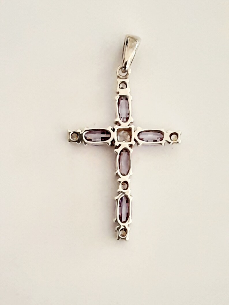 Pu&ograve; includere: Un ciondolo a forma di croce in argento con una pietra centrale trasparente e pietre viola intorno ai bordi.