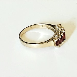 May include: A gold ring with a row of red gemstones and smaller clear gemstones set in the band. The ring is marked "14K" on the inside.