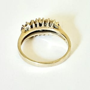 May include: A gold band ring with a row of small, clear stones set in the center.