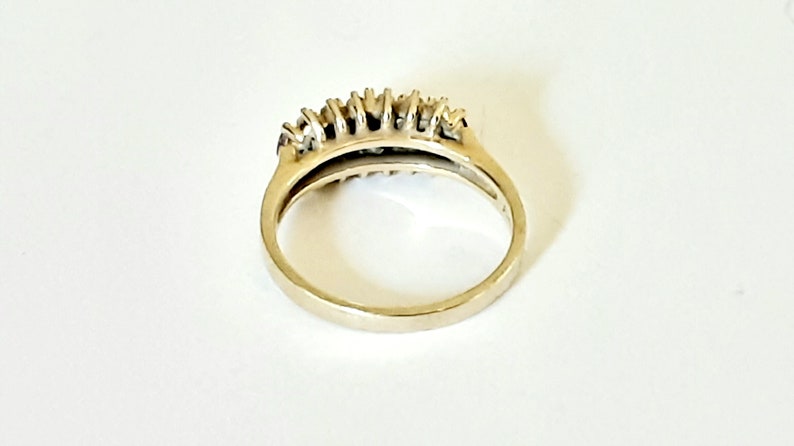 May include: A gold band ring with a row of small, clear stones set in the center.
