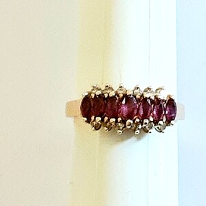 May include: A gold ring with a row of oval-shaped red gemstones surrounded by smaller white gemstones.