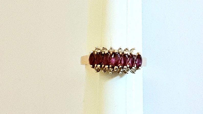 May include: A gold ring with a row of oval-shaped red gemstones surrounded by smaller white gemstones.