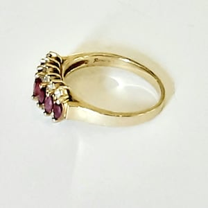 May include: A gold ring with a row of five oval-shaped red gemstones and smaller clear gemstones set in the band.