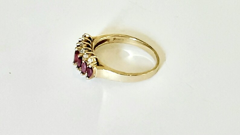 May include: A gold ring with a row of five oval-shaped red gemstones and smaller clear gemstones set in the band.