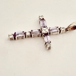 Pu&ograve; includere: Un ciondolo a forma di croce in argento con una grande pietra centrale trasparente e pietre pi&ugrave; piccole di colore viola intorno ai bordi.