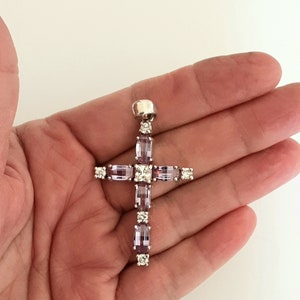 Pu&ograve; includere: Un ciondolo a forma di croce in argento con pietre preziose viola e trasparenti. La croce &egrave; incastonata con pietre rettangolari e quadrate.