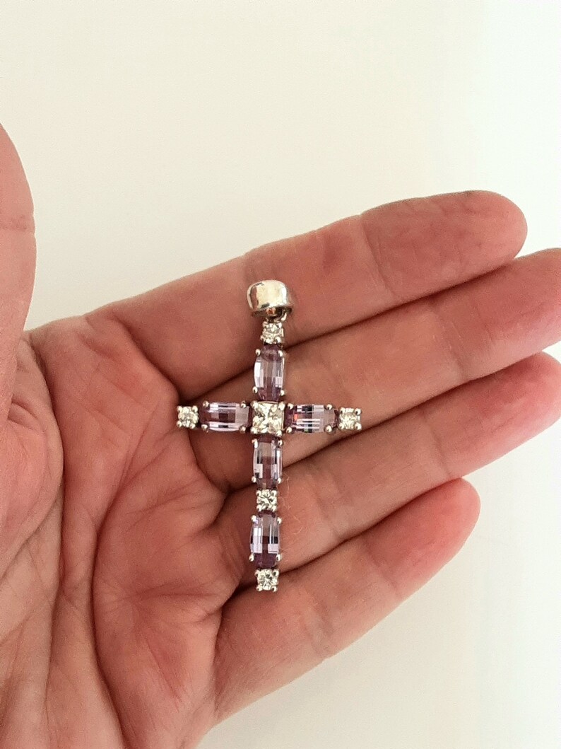 Pu&ograve; includere: Un ciondolo a forma di croce in argento con pietre preziose viola e trasparenti. La croce &egrave; incastonata con pietre rettangolari e quadrate.