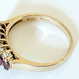 May include: A gold ring with a row of red gemstones and smaller white gemstones. The ring is marked "14K" and "THAILAND".