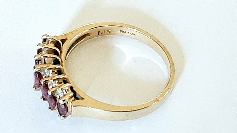 May include: A gold ring with a row of red gemstones and smaller white gemstones. The ring is marked "14K" and "THAILAND".