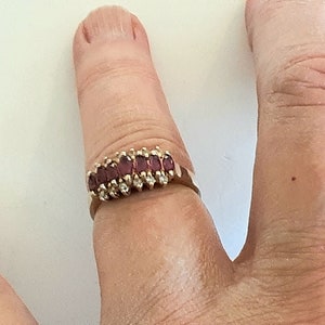May include: A gold ring with a row of red baguette-shaped gemstones set in a gold band.