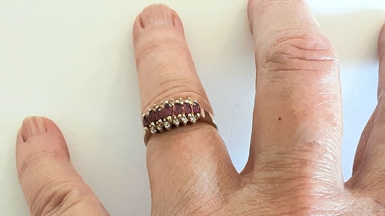 May include: A gold ring with a row of red baguette-shaped gemstones set in a gold band.