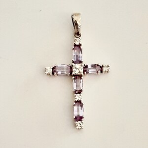 Pu&ograve; includere: Un ciondolo a forma di croce in argento con pietre preziose viola e trasparenti. La croce &egrave; incastonata con pietre rettangolari e quadrate.