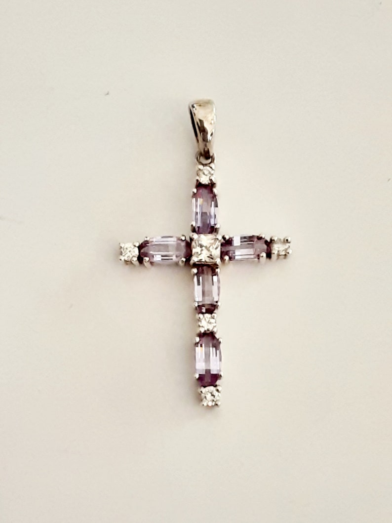 Pu&ograve; includere: Un ciondolo a forma di croce in argento con pietre preziose viola e trasparenti. La croce &egrave; incastonata con pietre rettangolari e quadrate.