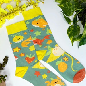 May include: A pair of green socks with a yellow cuff. The socks feature a variety of colorful cartoon designs, including fish, fruit, and stars.