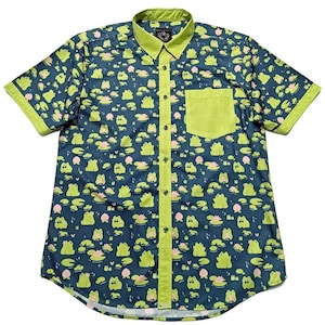 May include: A short-sleeved button-down shirt with a navy blue background and a repeating pattern of green frogs, lily pads, and pink flowers. The collar, pocket, and trim are a bright green. The shirt has a single pocket on the chest.