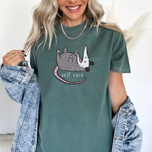 May include: A green t-shirt with a cartoon possum graphic and the text "self care".