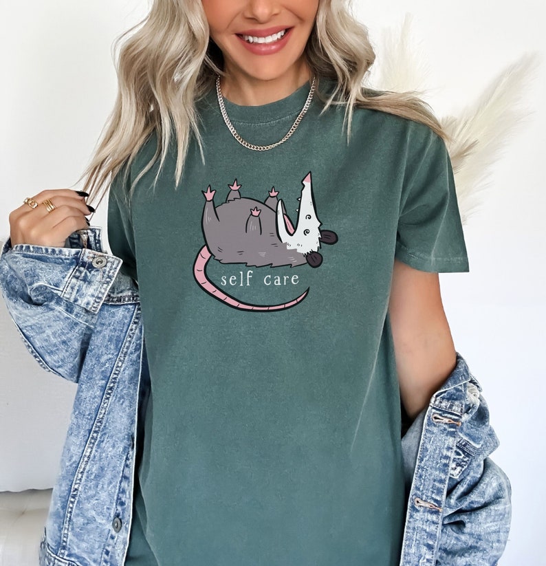 May include: A green t-shirt with a cartoon possum graphic and the text "self care".