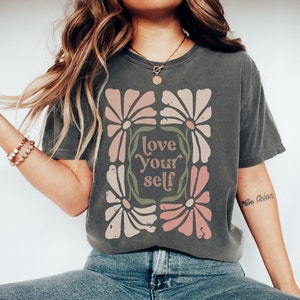 以下が含まれることがあります： レトロなフォントで「love your self」というテキストが書かれた、花柄のグレーのTシャツです。