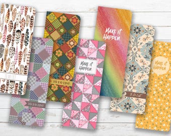 May include: A collection of six rectangular to-do list notepads featuring various patterns including feathers, patchwork squares, floral prints, and a rainbow gradient. Several pads display the text "Make it Happen" or "To Do List."