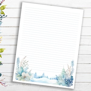 May include: A lined stationery sheet with a watercolor winter scene at the bottom. The design features blue and white flowers, pine trees, and a snowy landscape. The paper is set against a white wooden background.