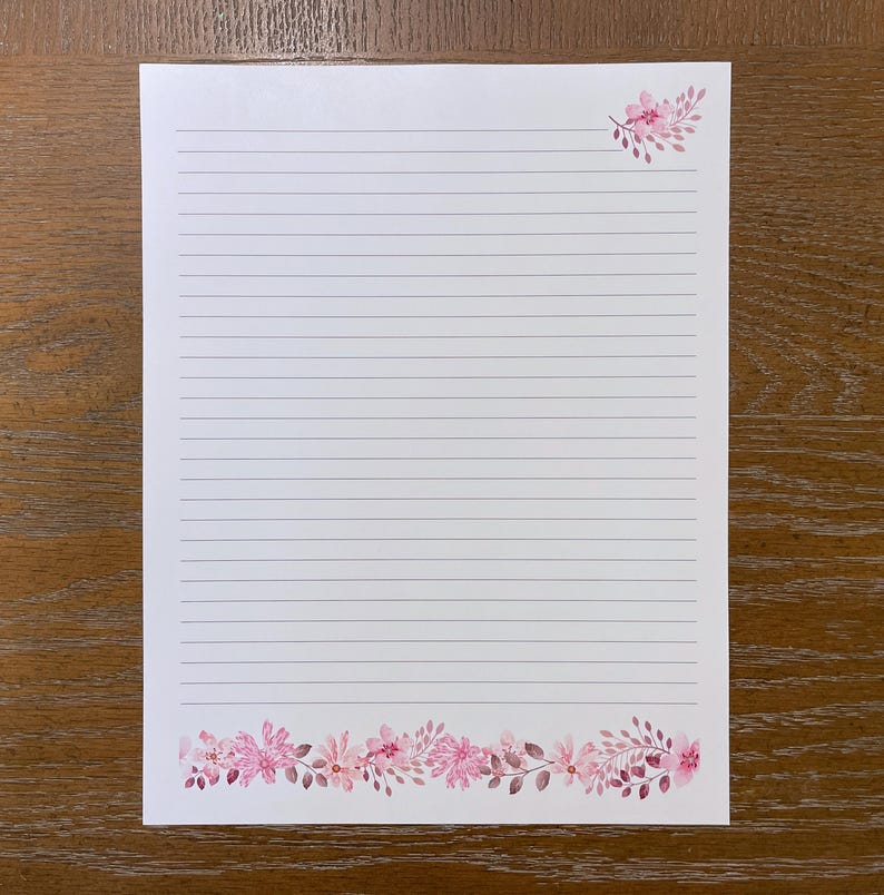 May include: A white sheet of lined stationery paper featuring a horizontal border of pink watercolor flowers and leaves at the bottom edge and a smaller matching floral cluster in the top right corner of the page.