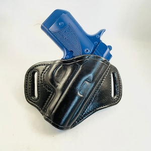 Peut inclure: Un étui en cuir noir avec un pistolet bleu à l'intérieur. L'étui a une boucle de ceinture et une fermeture à pression.