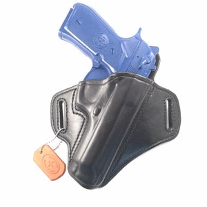 May include: A black leather holster with a blue handgun inside. The holster has a brown leather tag attached to it with the text "KUSTOM KRAFT HANDMADE" on it.
