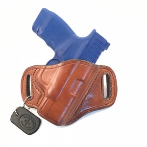 May include: A brown leather holster with a blue handgun inside. The holster has a metal tag attached to it that says "City Leather, handcrafted".