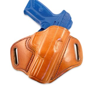 May include: A brown leather holster with a blue handgun inside. The holster has a belt loop and is designed for concealed carry.