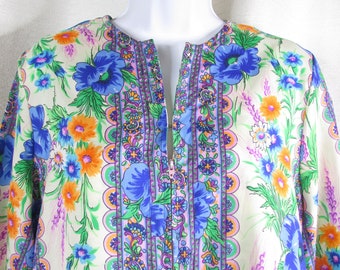 May include: A white, long-sleeved shirt with a floral print featuring blue, orange, and green flowers. The shirt has a zipper closure and a paisley-style border.