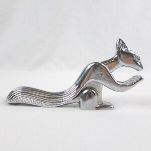 May include: A silver squirrel nutcracker with a detailed, textured tail and a hinged jaw. The nutcracker is in a crouching position, ready to crack nuts.