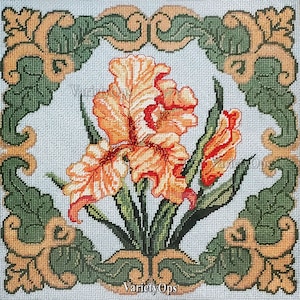 May include: Needlepoint design featuring a central cluster of orange and red iris flowers with green leaves. The flowers are set against a light blue background, framed by a green and gold decorative border. The text "VarietyOps" is at the bottom.