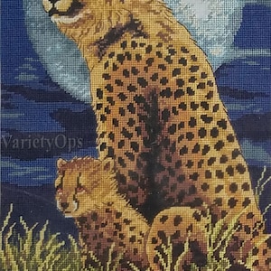 May include: A needlepoint tapestry featuring a large cheetah and a smaller cheetah cub sitting in tall green grass. The background displays a large, pale full moon against a dark blue night sky. The text VarietyOps is visible on the image.