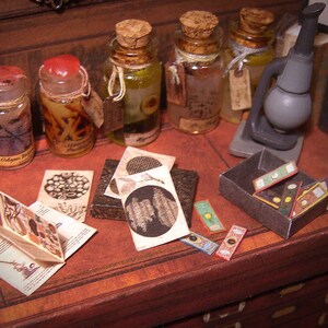 Puede incluir: Una mesa de madera en miniatura con una colección de botellas de vidrio, un microscopio y una caja de pequeñas tarjetas de colores. Las botellas están llenas de varios líquidos y tienen etiquetas con texto. La mesa tiene un cajón con una manija de madera.