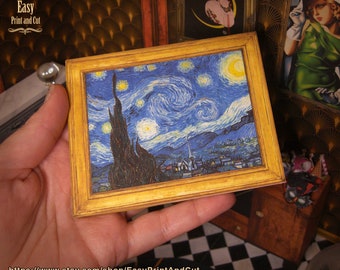 May include: Miniature framed print of Van Gogh's "Starry Night" painting. The artwork depicts a swirling blue night sky with yellow stars and a crescent moon. The frame is gold-coloured, and the print is held in a hand.