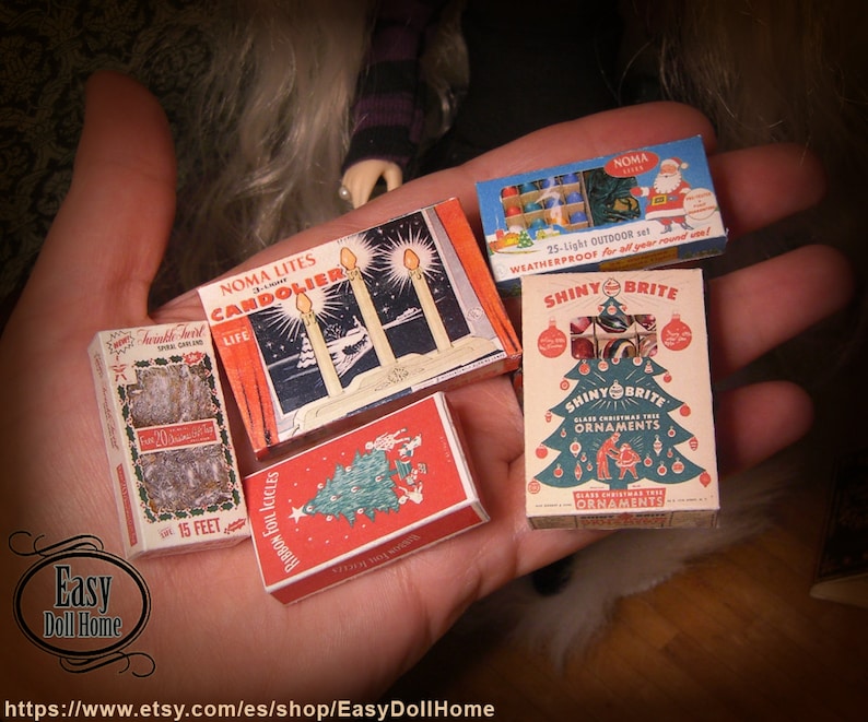 K&ouml;nnte beinhalten: Eine Sammlung von Vintage-Weihnachtsdekorationen in Miniaturboxen. Die Boxen sind rot, gr&uuml;n und wei&szlig; mit Bildern von Weihnachtslichtern, Kugeln und einem Weihnachtsbaum. Der Text auf den Boxen lautet "Noma Lites Candoler", "Shiny Brite" und "Shiny Brite Ornaments".
