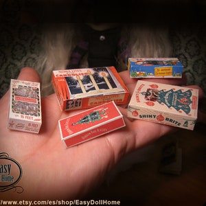 K&ouml;nnte beinhalten: Vier Miniaturboxen mit Vintage-Weihnachtsdekoration. Die Boxen sind rot, wei&szlig; und gr&uuml;n mit Bildern von Weihnachtsb&auml;umen, Kerzen und Ornamenten. Die Boxen sind mit "Noma Lites Candoliers", "Shiny Brite" und "Ribbon Foil Icicles" beschriftet.