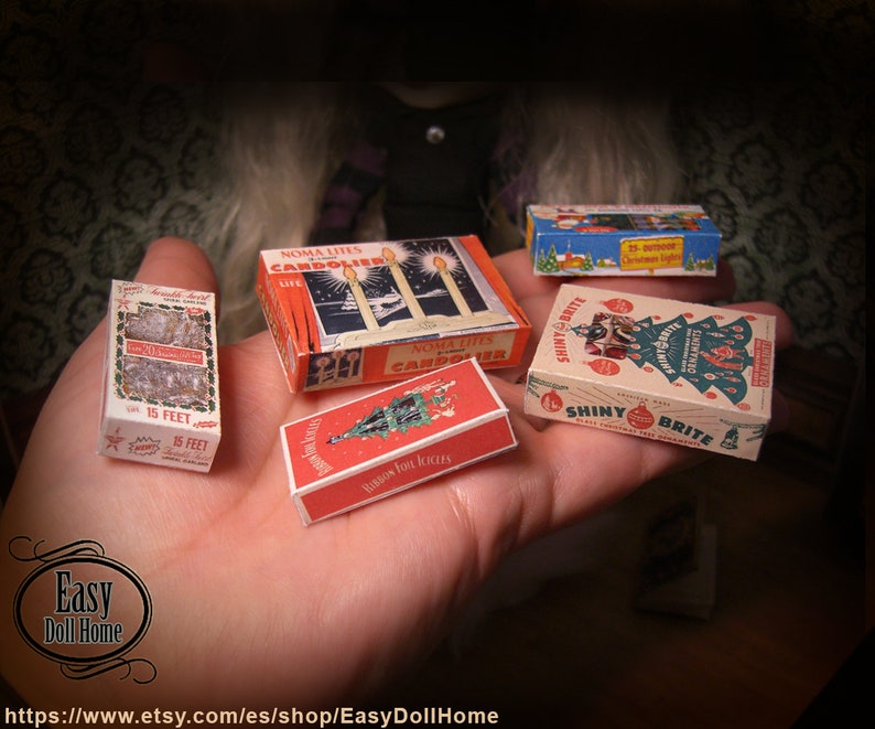 K&ouml;nnte beinhalten: Vier Miniaturboxen mit Vintage-Weihnachtsdekoration. Die Boxen sind rot, wei&szlig; und gr&uuml;n mit Bildern von Weihnachtsb&auml;umen, Kerzen und Ornamenten. Die Boxen sind mit "Noma Lites Candoliers", "Shiny Brite" und "Ribbon Foil Icicles" beschriftet.