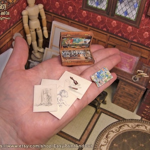 Peut inclure: Une petite boîte d'artiste en bois ouverte, révélant de minuscules fournitures d'art. Plusieurs petits croquis et une palette colorée sont tenus à proximité. La scène se déroule dans une pièce miniature détaillée, avec le texte "Easy Print and Cut".
