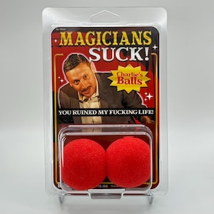 May include: A novelty item packaged in a clear plastic blister pack. The packaging features a man in a suit and the text "MAGICIANS SUCK!" and "YOU RUINED MY FUCKING LIFE!". Two red sponge balls are visible.