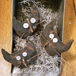 May include: Three black felt cat ornaments with button eyes and twig noses are nestled in a galvanized metal container filled with white Spanish moss.