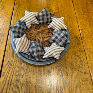 May include: A blue and white striped and plaid fabric star ornaments arranged in a circle on a blue metal tray.