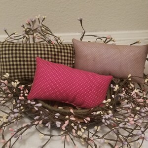 Puede incluir: Tres almohadas decorativas con diferentes patrones. Las almohadas est&aacute;n dispuestas en una cesta de mimbre marr&oacute;n con una corona de ramas de bayas blancas y moradas.