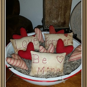 May include: A white bowl with a red rim filled with red and white striped fabric hearts and fabric pillows with the words "Love", "Forever", and "Be Mine" embroidered on them.